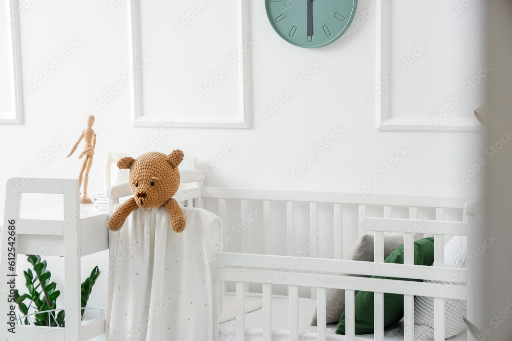 Baby crib with toy bear in light bedroom