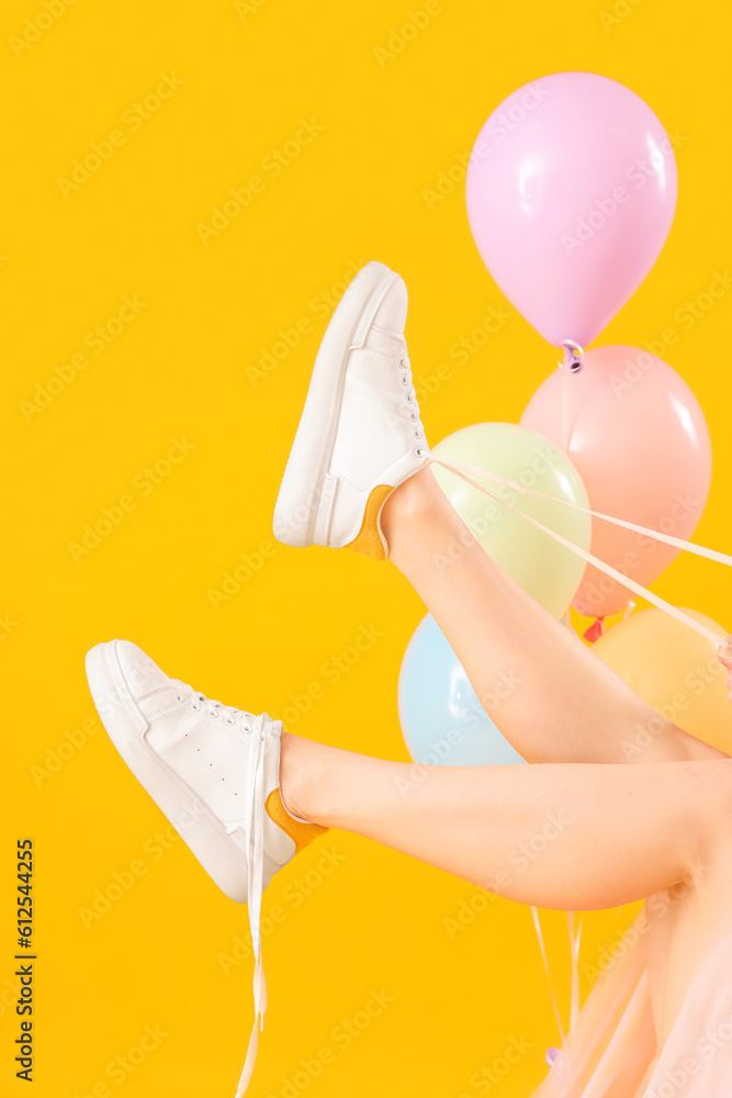 Young woman tying shoes laces with balloons on yellow background