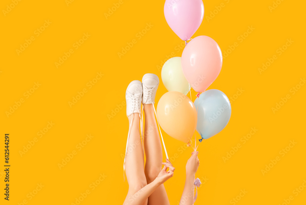 Young woman tying shoes laces with balloons on yellow background