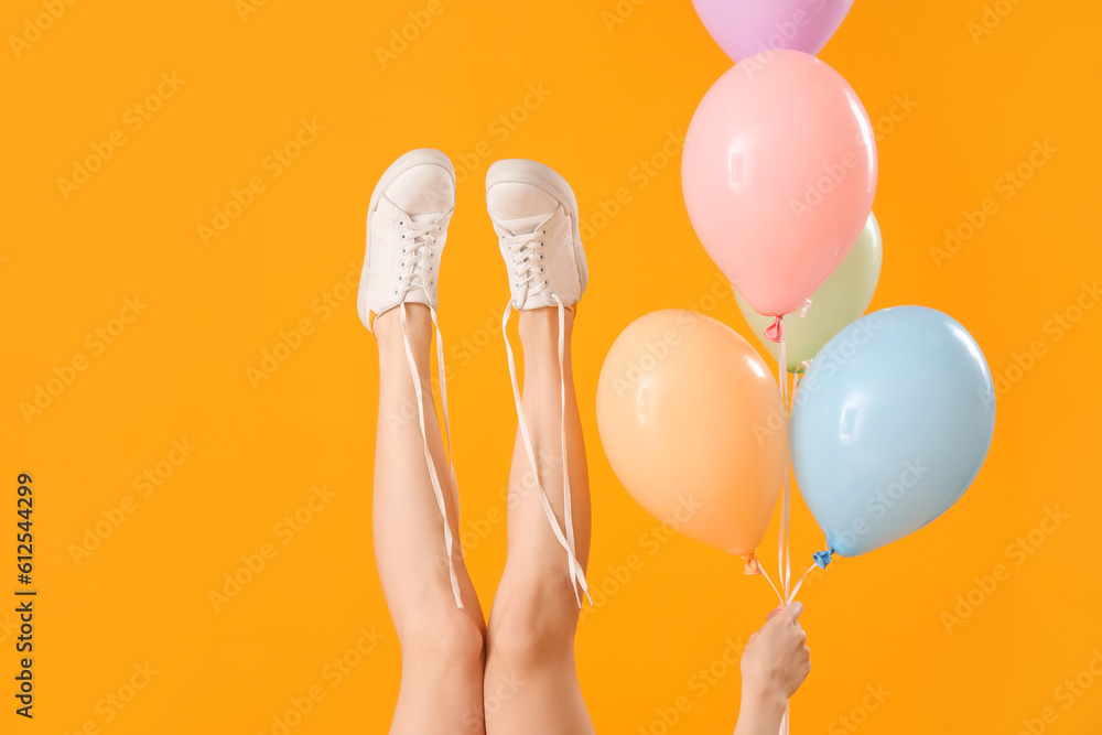 Female legs with undone shoes laces and balloons on yellow background