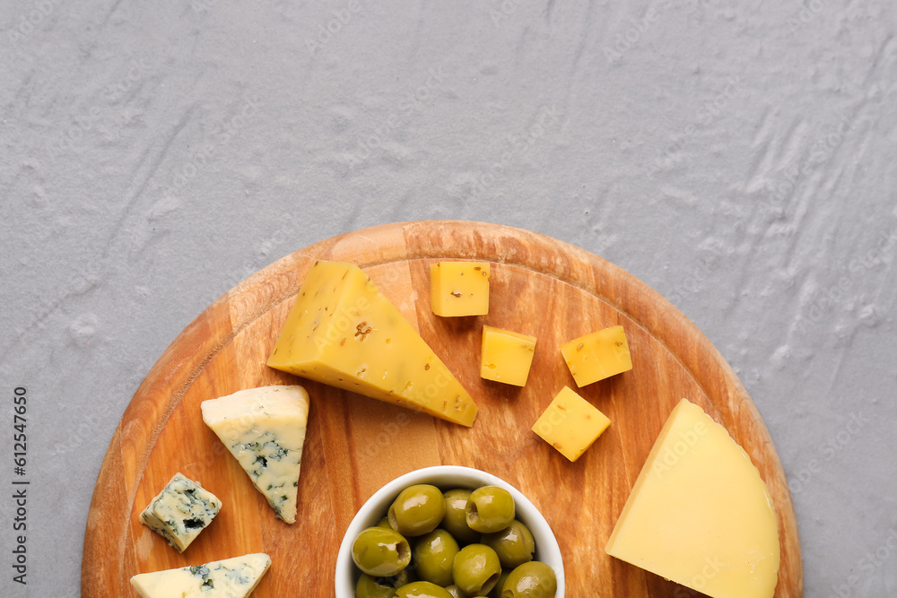 Wooden board with pieces of tasty cheese on grey background, closeup