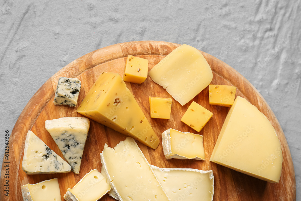 Wooden board with pieces of tasty cheese on grey background, closeup