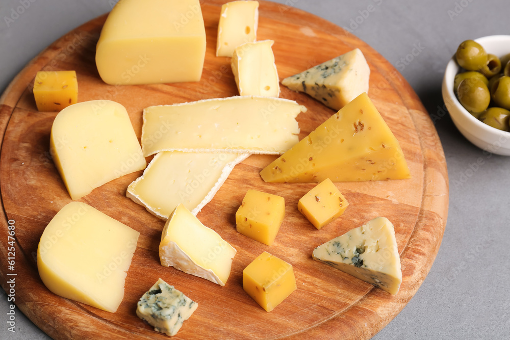 Wooden board with pieces of tasty cheese on grey background