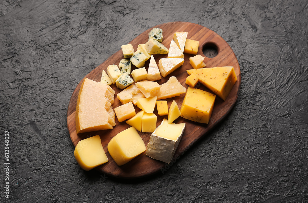 Wooden board with pieces of tasty cheese on dark background