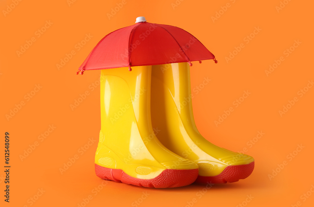 Creative composition with gumboots and mini umbrella on orange background