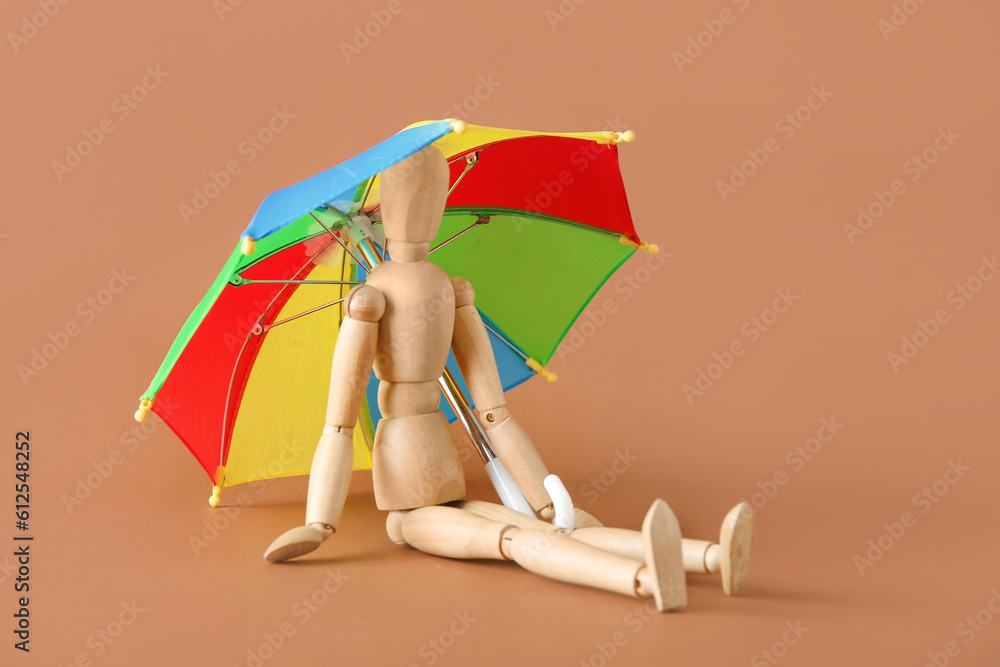 Creative composition with wooden mannequin and mini umbrella on brown background