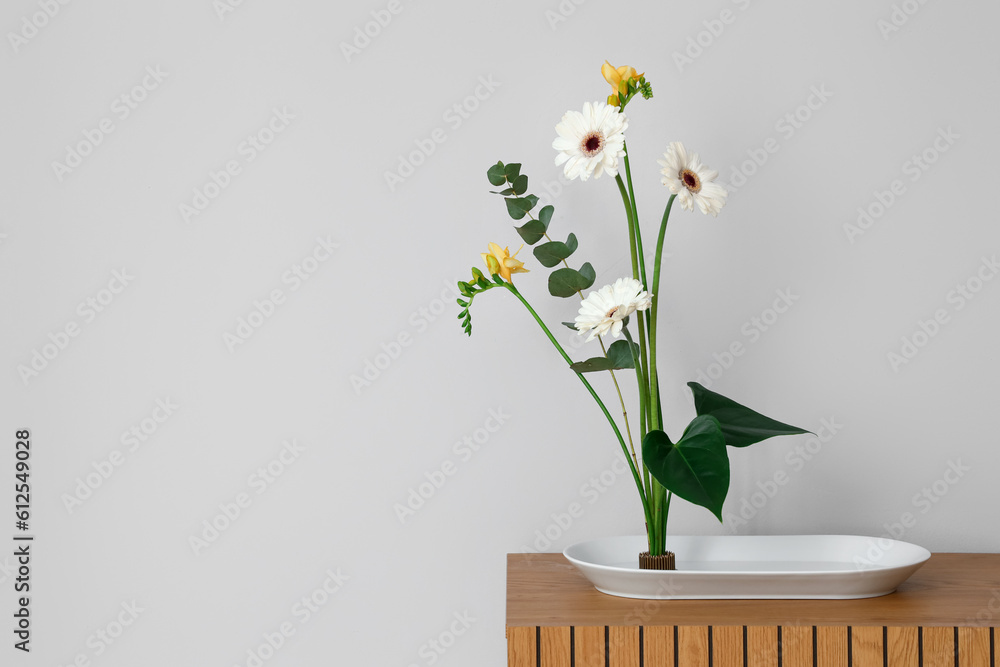 Beautiful ikebana on table near light wall