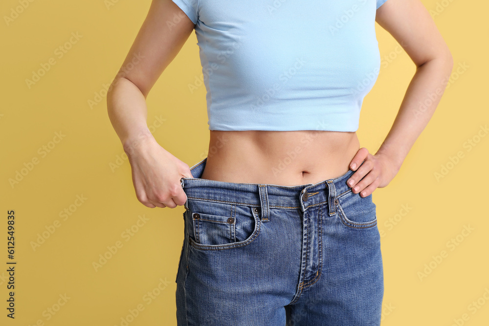 Young woman in loose jeans on beige background. Diet concept