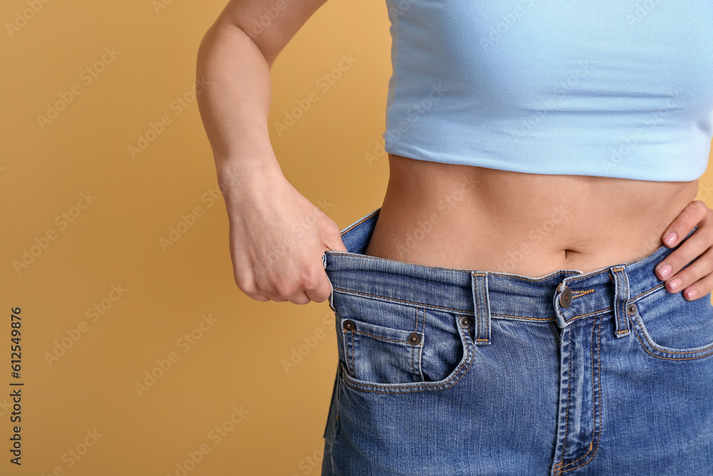 Young woman in loose jeans on beige background, closeup. Diet concept