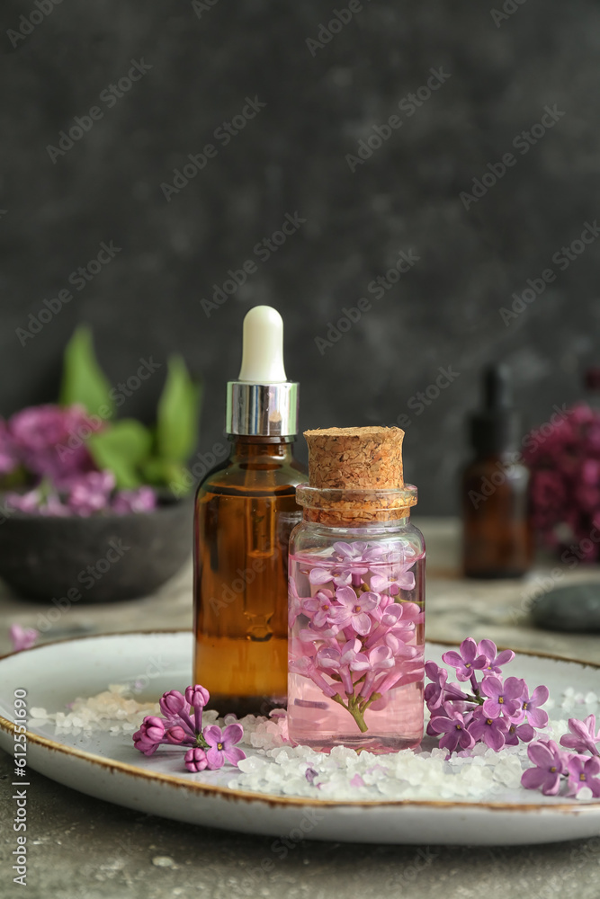 Bottles of cosmetic oil with beautiful lilac flowers and sea salt on grey table