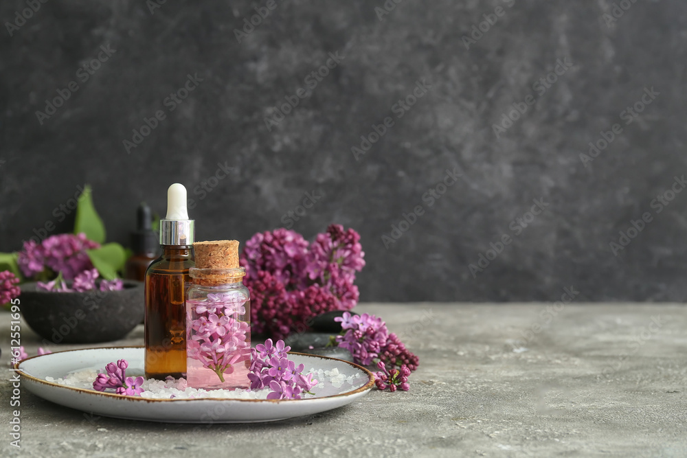 Bottles of cosmetic oil with beautiful lilac flowers and sea salt on grey table