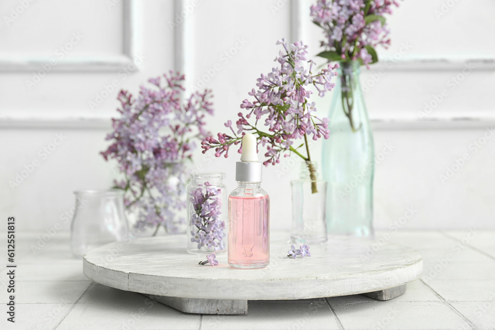 Bottles of cosmetic oil with beautiful lilac flowers on white table