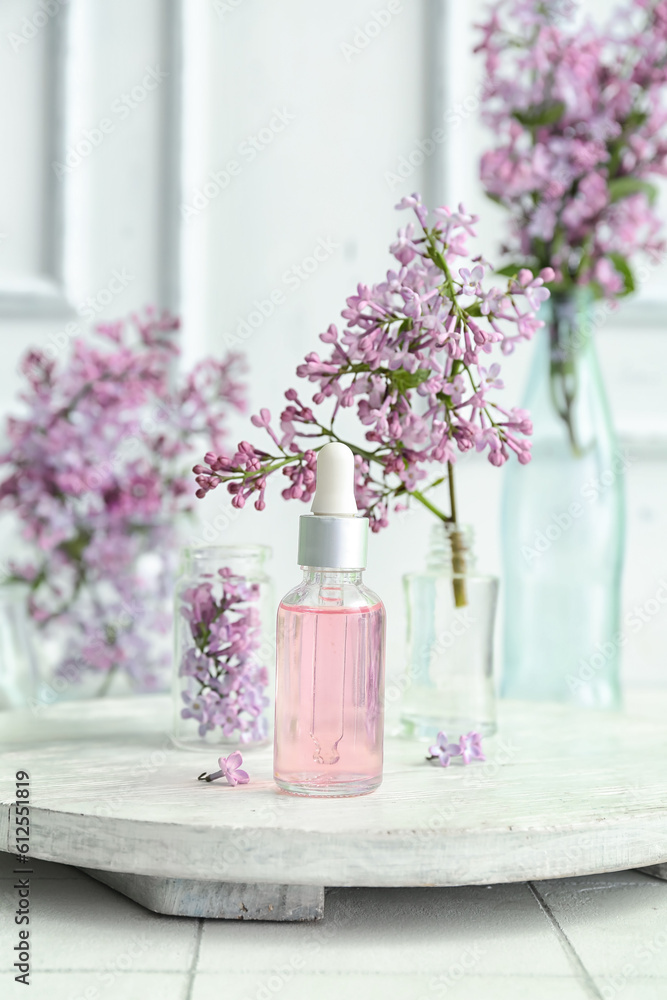 Bottles of cosmetic oil with beautiful lilac flowers on white table