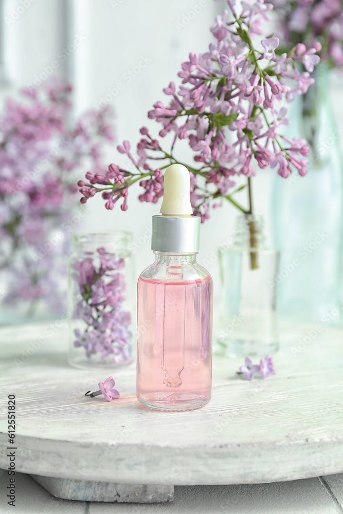 Bottles of cosmetic oil with beautiful lilac flowers on white table