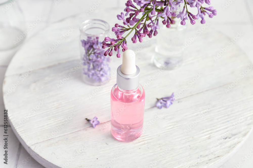 Bottles of cosmetic oil with beautiful lilac flowers on white table