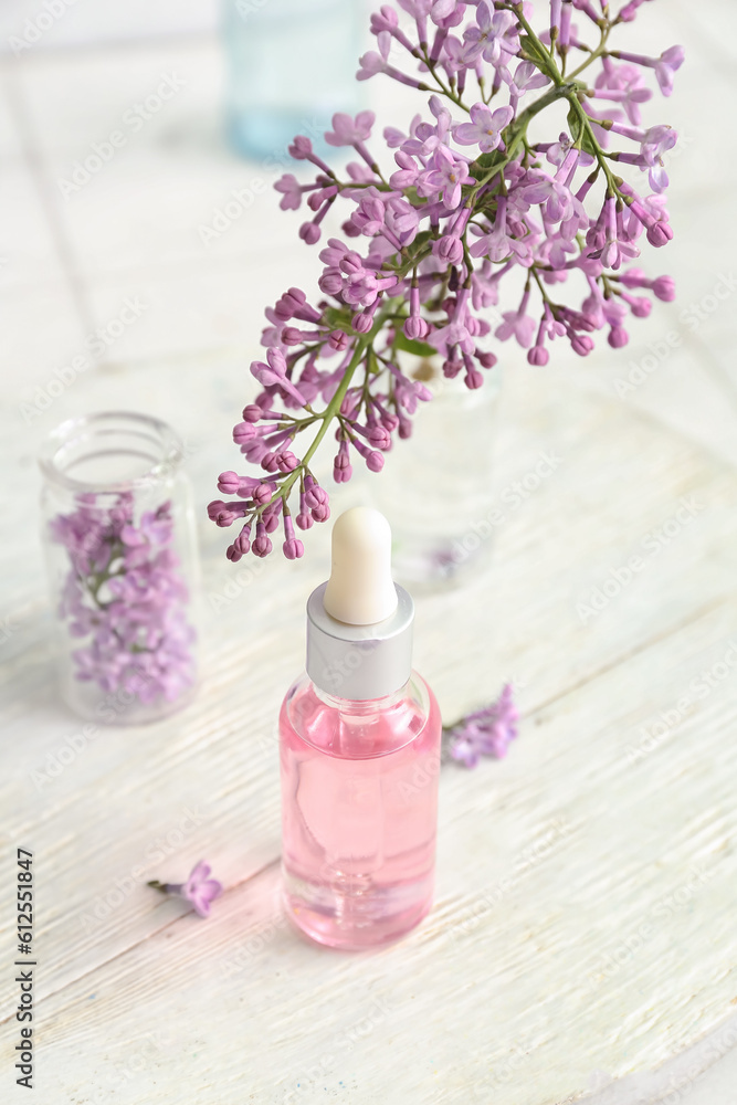 Bottles of cosmetic oil with beautiful lilac flowers on white table