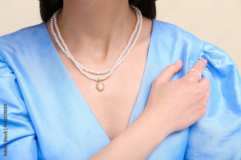 Beautiful young woman with stylish necklaces near beige wall