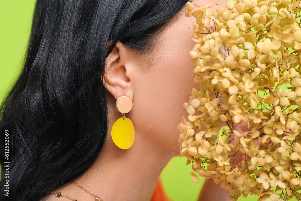 Profile of young woman wearing stylish jewelry with flowers near green wall