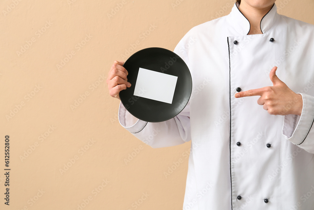 Female chef holding plate with blank card on beige background