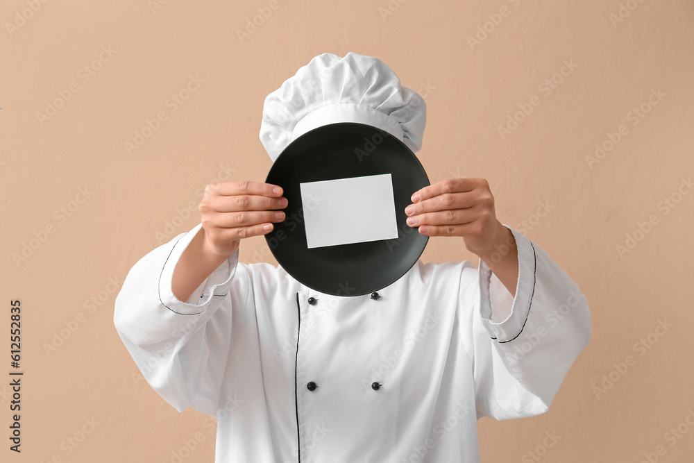 Female chef holding plate with blank card on beige background