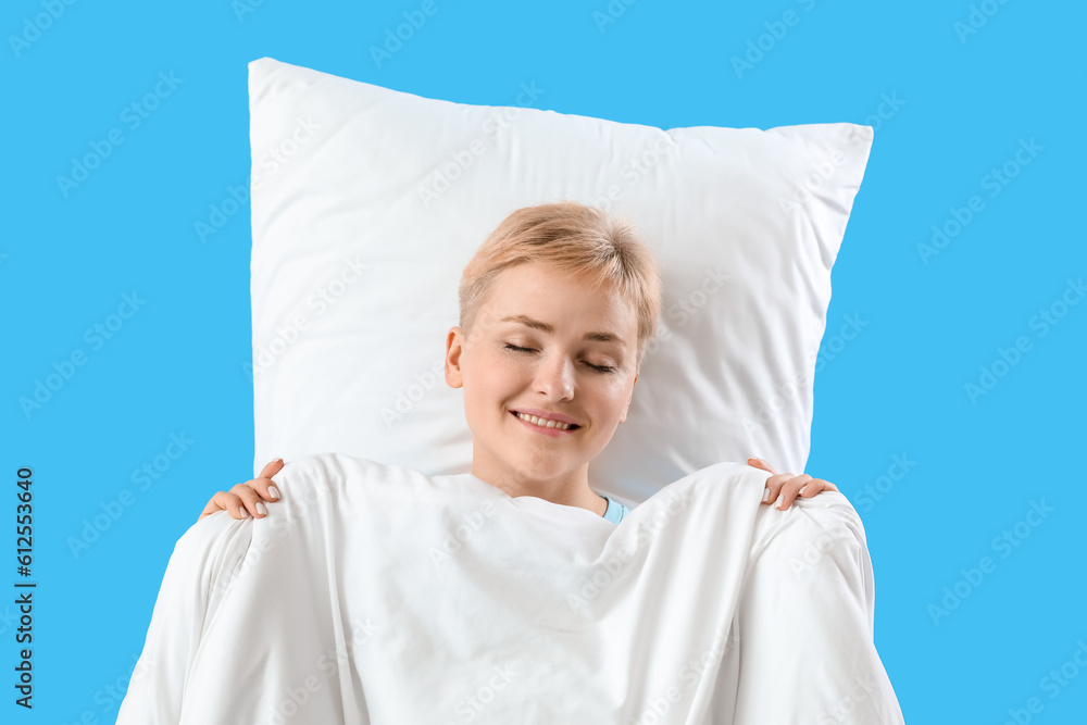 Young woman with soft blanket and pillow sleeping on blue background