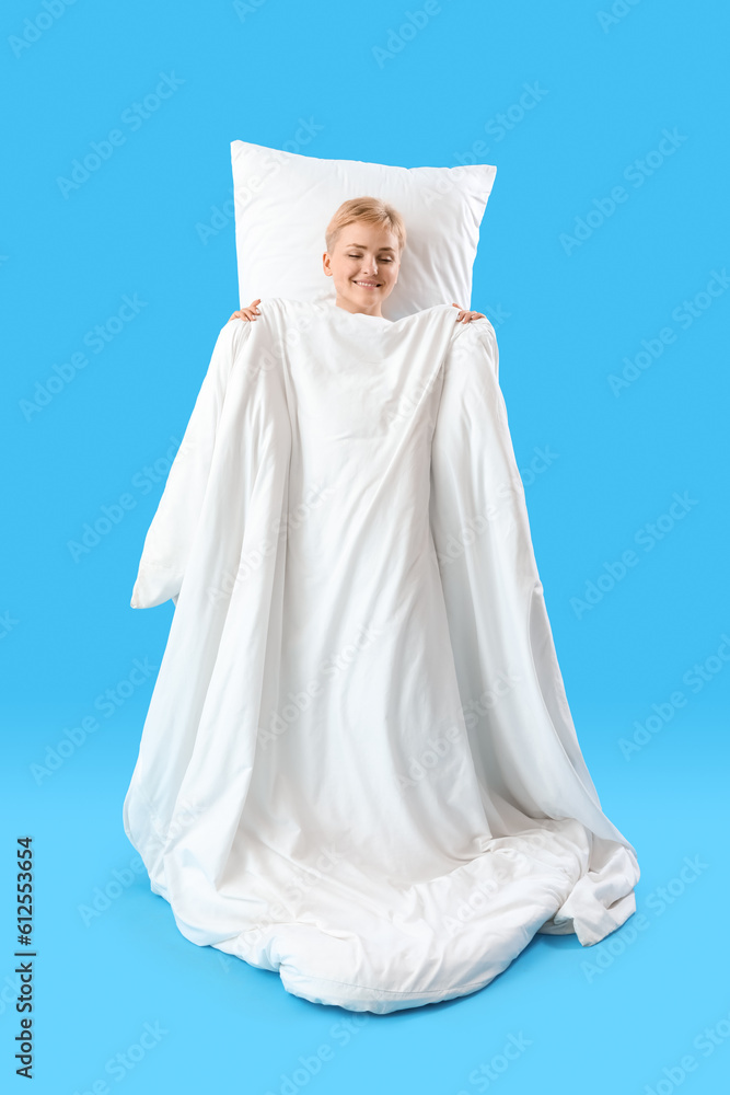 Young woman with soft blanket and pillow sleeping on blue background