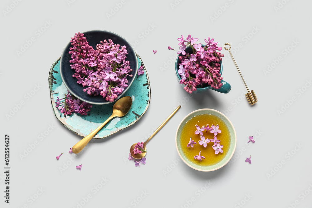 Bowl of honey with cup of lilac flowers on white background