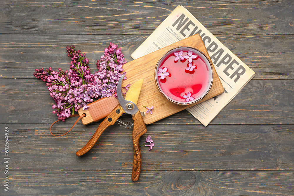 Cup of tea with lilac and garden pruners on wooden table