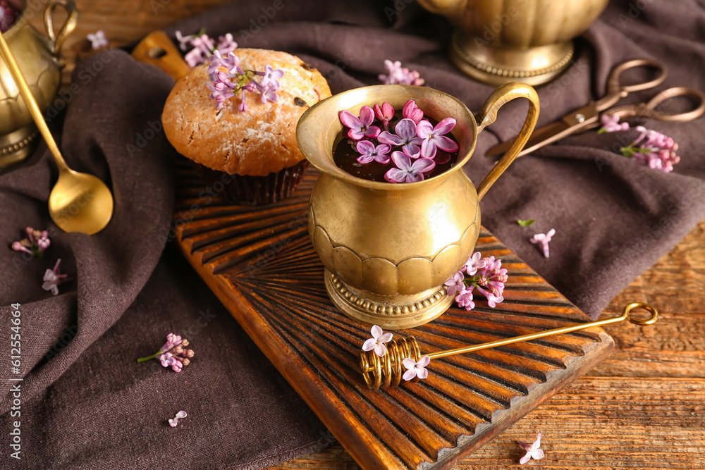 Lilac flowers in jug and cupcake on wooden table