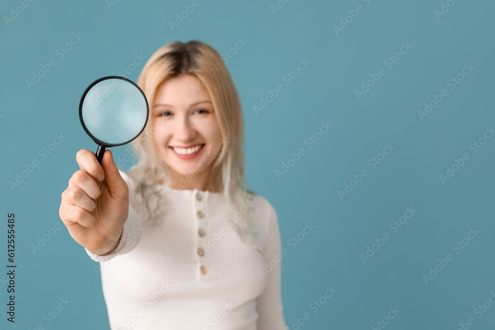 Young woman with magnifier on blue background, closeup