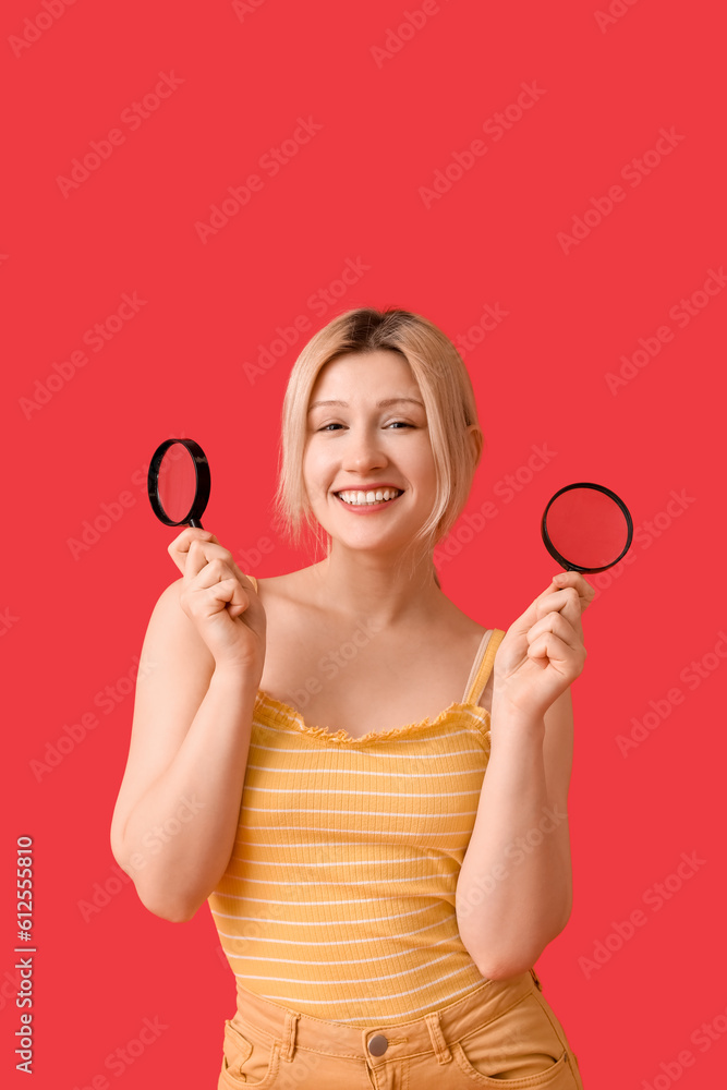 Young woman with magnifiers on red background