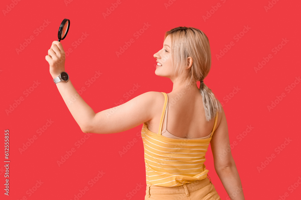 Young woman with magnifier on red background