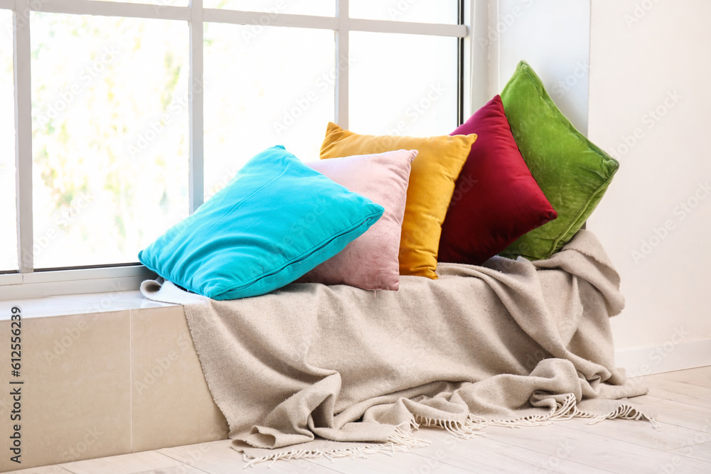 Colorful pillows with plaid on windowsill in room