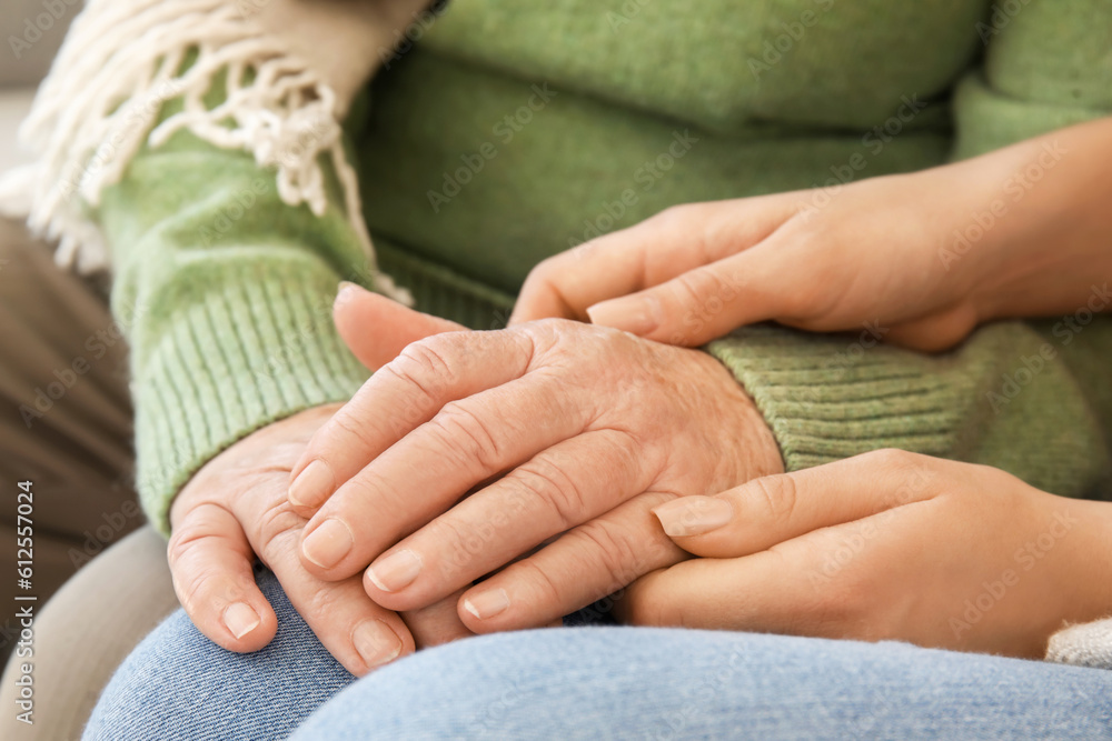 Senior woman with her granddaughter holding hands at home, closeup