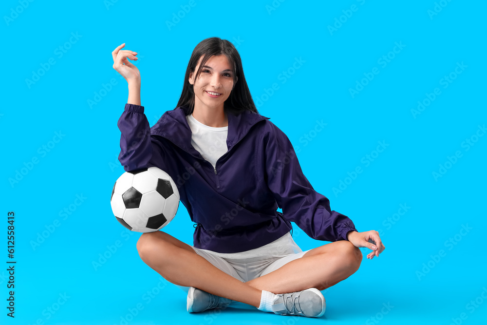 Young woman with soccer ball on blue background