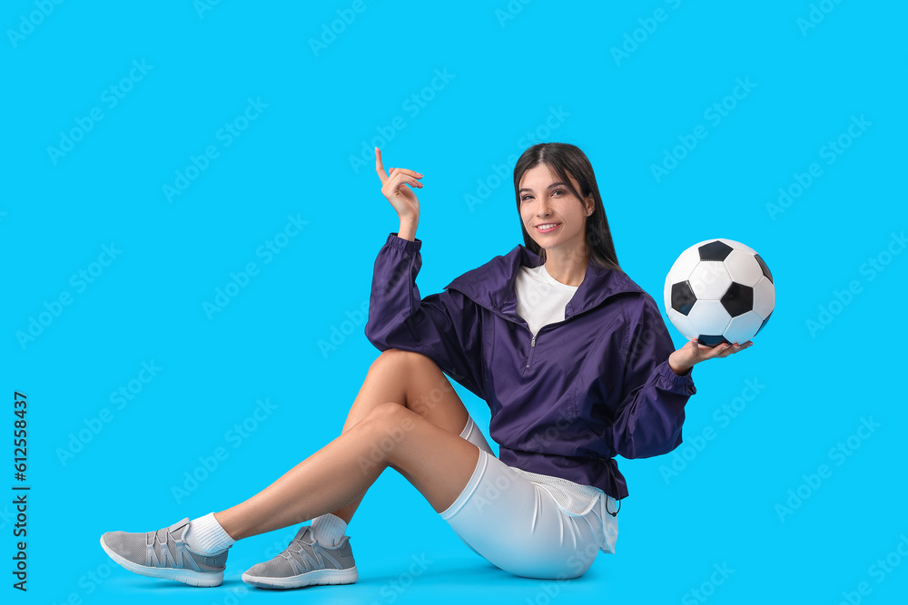 Young woman with soccer ball on blue background