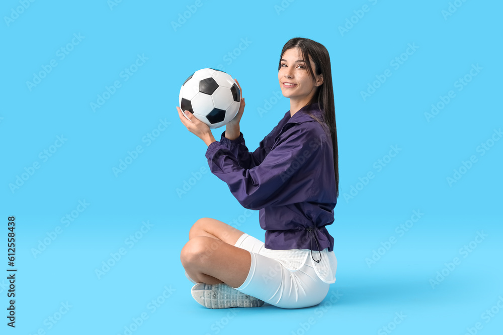 Young woman with soccer ball on blue background