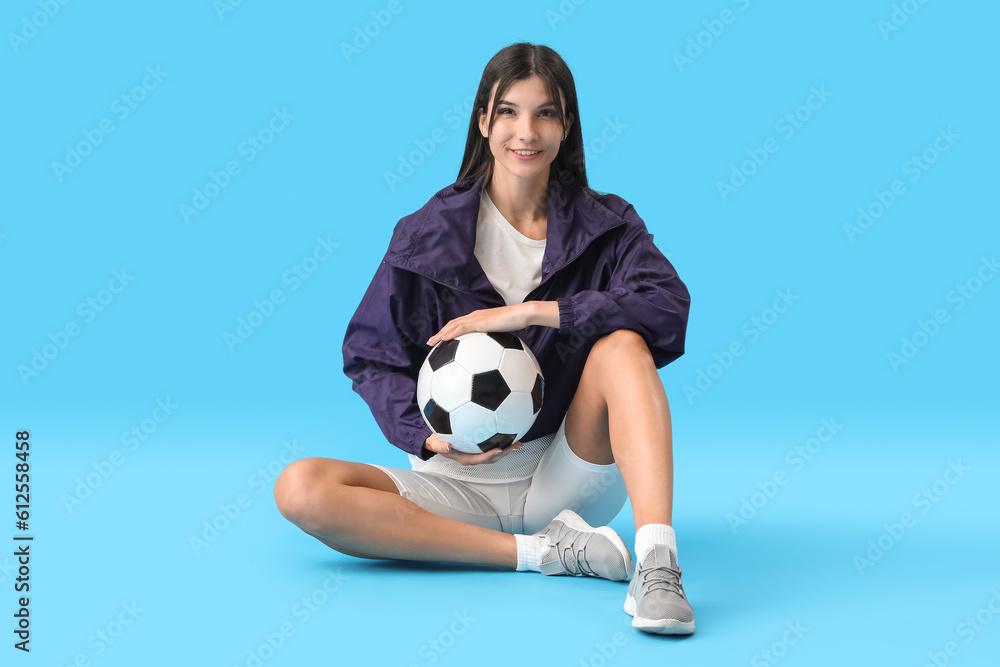 Young woman with soccer ball on blue background