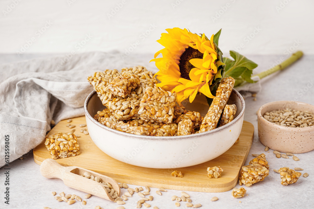 Board with bowls of tasty kozinaki, sunflower and seeds on white background