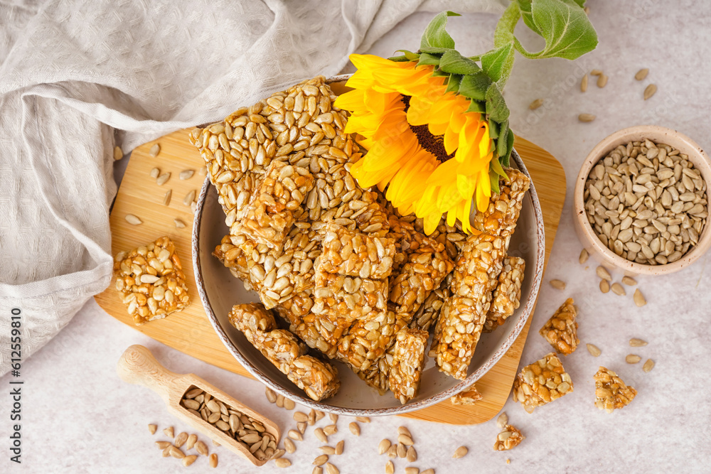 Board with bowls of tasty kozinaki, sunflower and seeds on white background