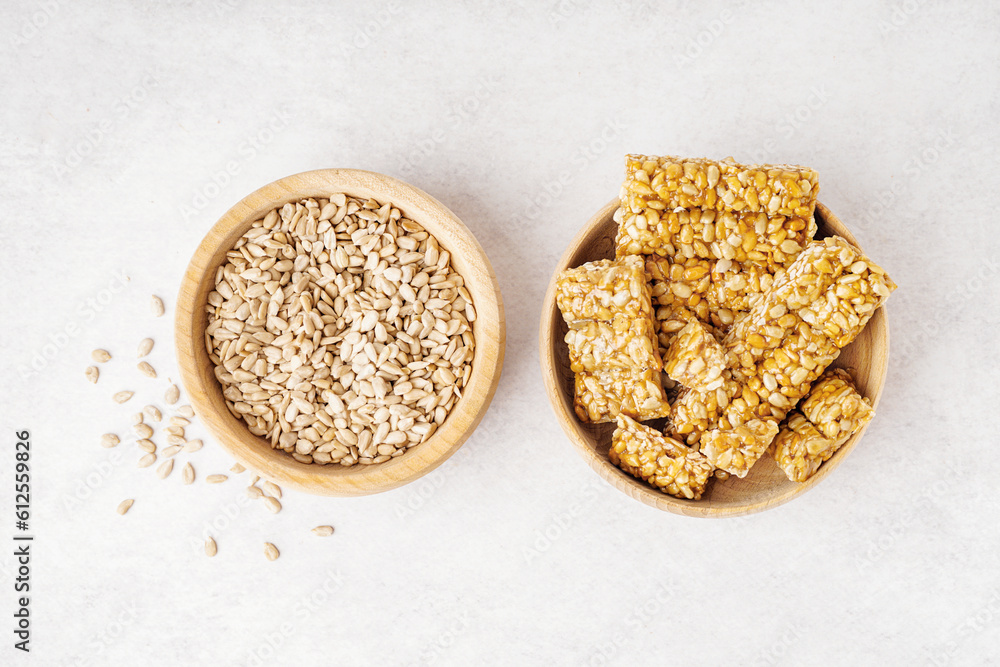 Bowls of tasty kozinaki and sunflower seeds on white background