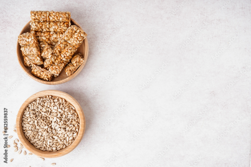 Bowls of tasty kozinaki and sunflower seeds on white background