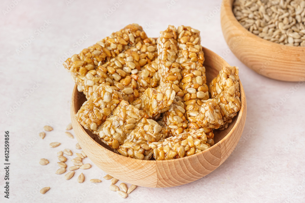 Bowls of tasty kozinaki and sunflower seeds on white background