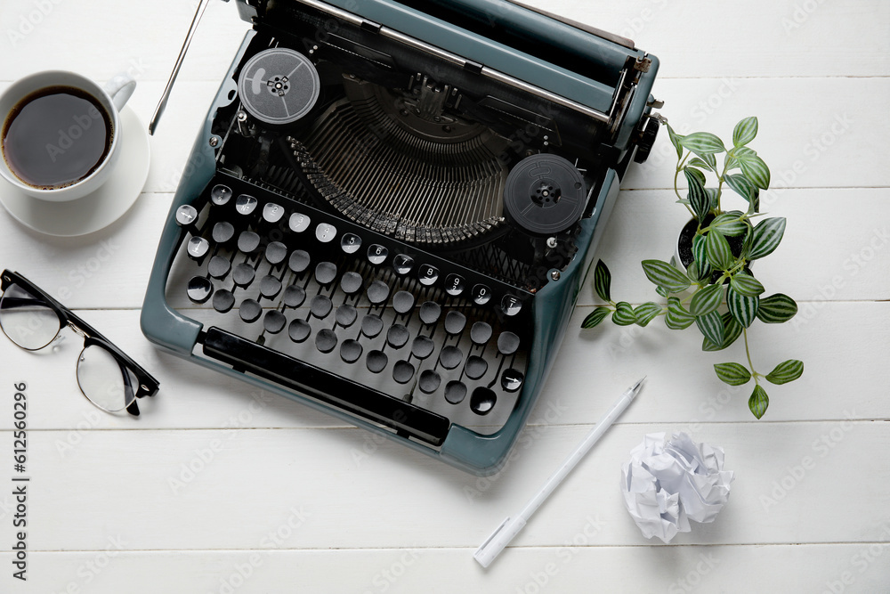 Vintage typewriter with cup of coffee, eyeglasses and houseplant on white wooden background