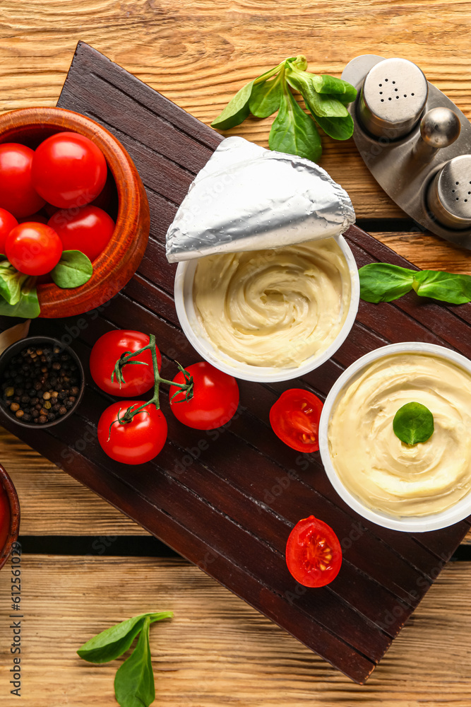 Board with boxes of processed cheese, basil and tomatoes on brown wooden background