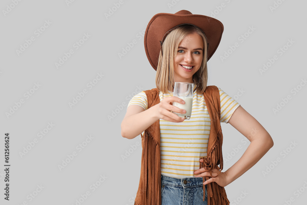 Beautiful cowgirl with glass of milk on grey background