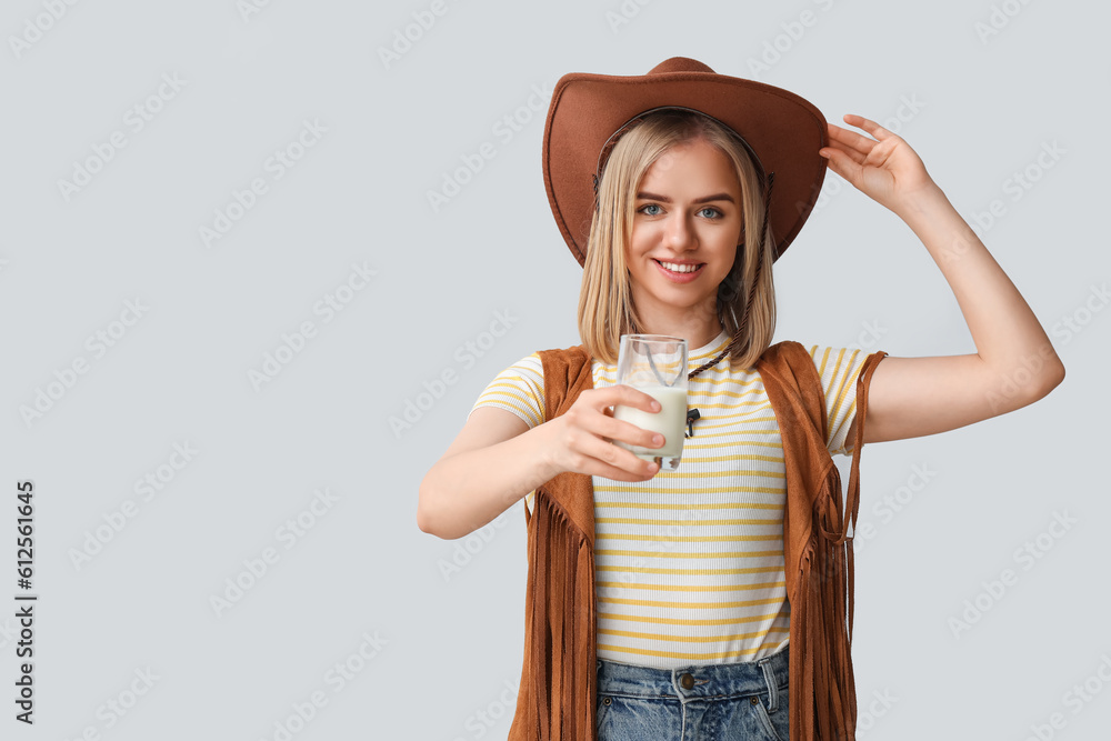 Beautiful cowgirl with glass of milk on grey background