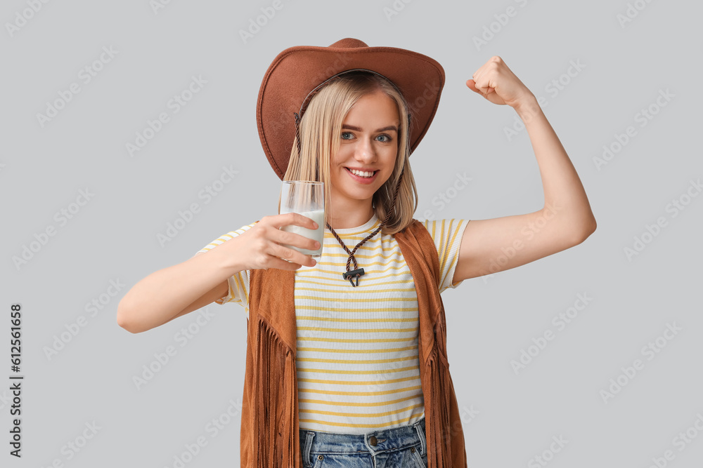 Beautiful cowgirl with glass of milk on grey background