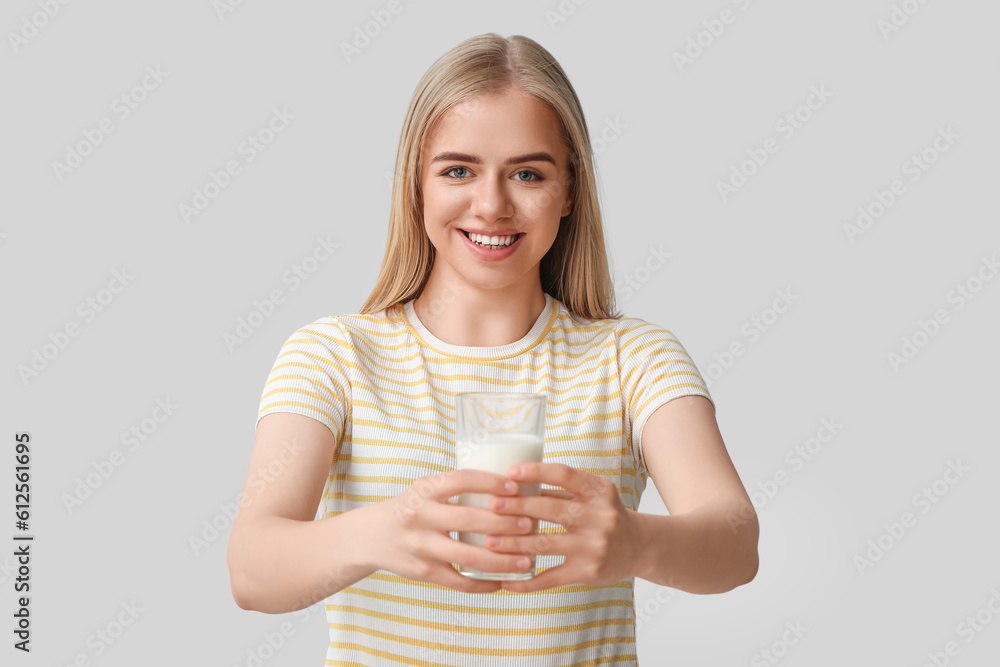 Beautiful young woman with glass of milk on grey background