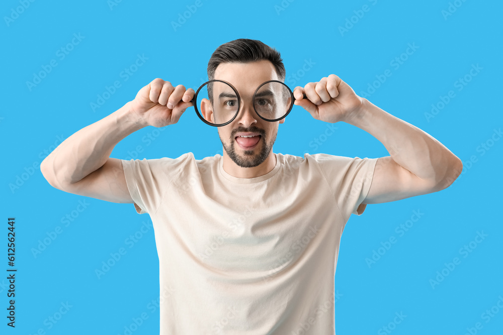 Handsome man with magnifiers showing tongue on blue background